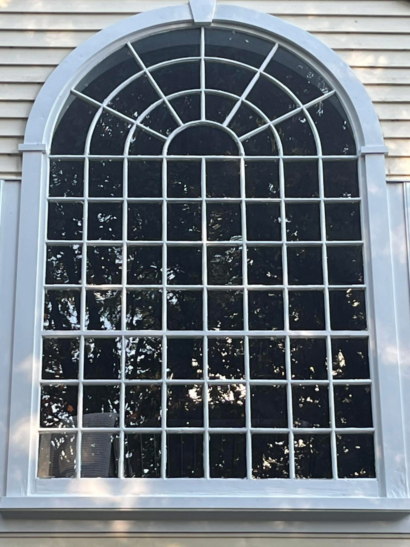 Restored arched multi-pane window with crisp hand-painted white trim on clapboard siding