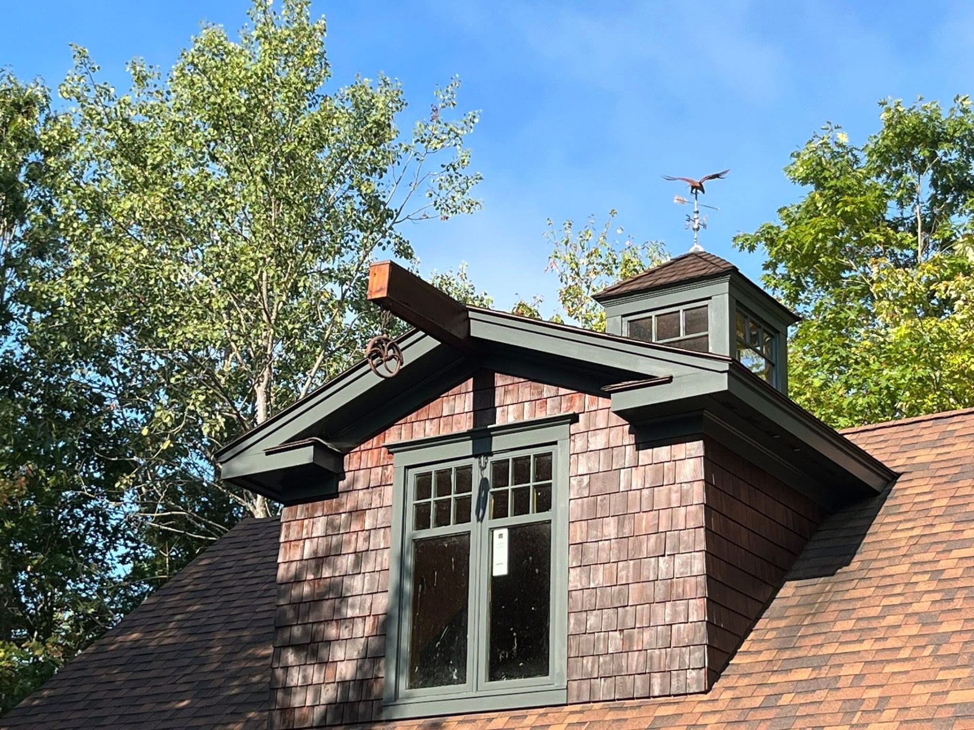 Cedar-shingled dormer and cupola with freshly painted dark green trim against a blue sky