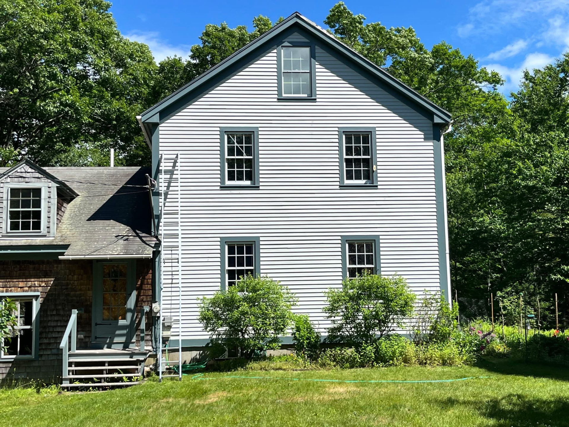 Two-story clapboard home freshly painted in light gray with slate blue window trim