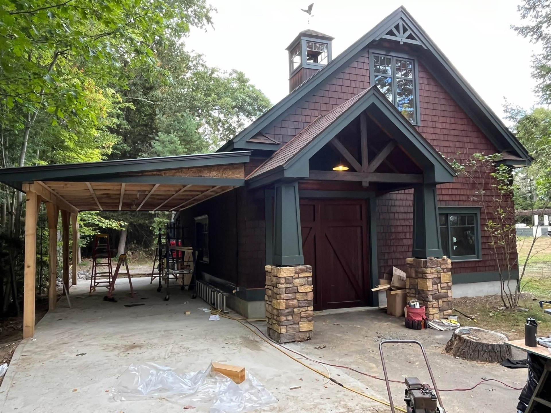 Cedar-shingled carriage house stained deep red with dark green trim and a matching carriage door