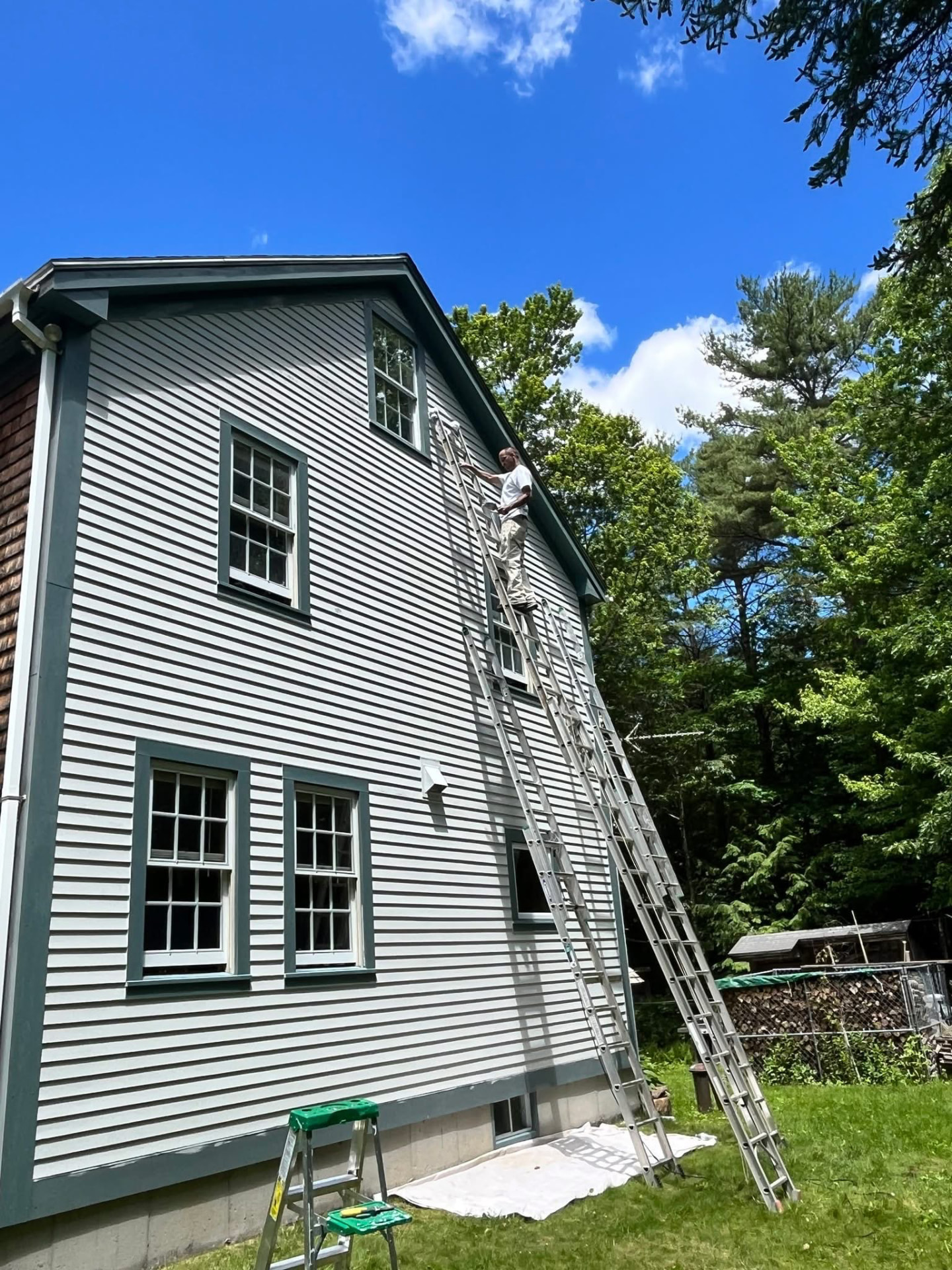 TD Painting crew member on an extension ladder painting second-story siding and trim