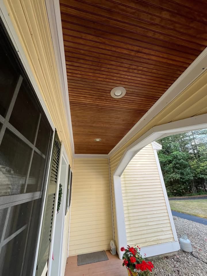 Covered porch with a dated stained wood ceiling and weathered cream siding before painting